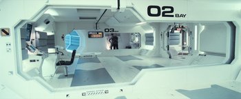 Movie still from “Moon” (2009), directed by Duncan Jones – A man standing inside of a room in a spaceship; Wide shot, Overhead angle