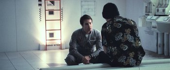 Movie still from “Moon” (2009), directed by Duncan Jones – A man and a woman sitting on the ground; Medium shot, Over the shoulder angle