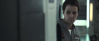 Movie still from “Moon” (2009), directed by Duncan Jones – A man standing in front of a mirror in front of a wall; Close Up shot, Over the shoulder angle