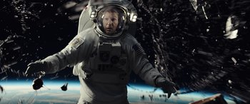 Movie still from “Moonfall” (2022), directed by Roland Emmerich – A man in a spacesuit standing in front of the earth; Medium shot, Overhead angle