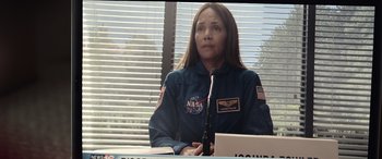 Movie still from “Moonfall” (2022), directed by Roland Emmerich – A woman in a nasa uniform sitting in front of a microphone; Medium shot, Over the shoulder angle