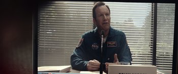 Movie still from “Moonfall” (2022), directed by Roland Emmerich – A man sitting in front of a microphone at a table; Close Up shot, Over the shoulder angle