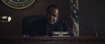Movie still from “Moonfall” (2022), directed by Roland Emmerich – A judge sitting at a desk in front of a microphone; Medium shot, Low angle