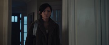 Movie still from “Moonfall” (2022), directed by Roland Emmerich – A woman in a brown coat holding a bag in front of a window; Medium shot, Over the shoulder angle