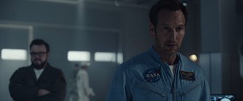Movie still from “Moonfall” (2022), directed by Roland Emmerich – A man wearing a nasa jacket standing in a room; Close Up shot, Over the shoulder angle