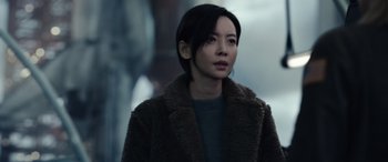 Movie still from “Moonfall” (2022), directed by Roland Emmerich – A woman in a brown coat looking to her left; Close Up shot, Over the shoulder angle