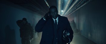 Movie still from “Moonfall” (2022), directed by Roland Emmerich – A man wearing a suit and tie holding a cell phone; Medium shot, Low angle