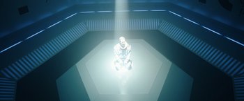 Movie still from “Moonfall” (2022), directed by Roland Emmerich – A man kneeling down in a room with a light shining on him; Wide shot, High angle