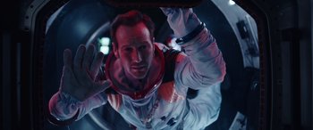 Movie still from “Moonfall” (2022), directed by Roland Emmerich – A man in a spacesuit is looking at the camera; Medium shot, Overhead angle