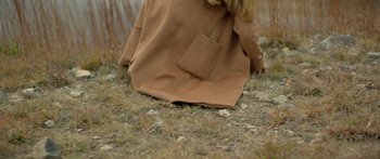 Movie still from “Moonrise” (2022), directed by Vickie Bronaugh – A woman in a brown coat sitting on the ground; Medium shot, High angle