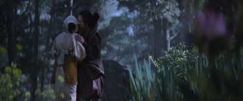 Movie still from “Mortal Kombat” (2021), directed by Simon McQuoid – A woman and a child are hugging in a forest; Medium shot, Over the shoulder angle