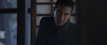 Movie still from “Mortal Kombat” (2021), directed by Simon McQuoid – A man wearing a black robe standing in front of a wooden wall; Close Up shot, Low angle