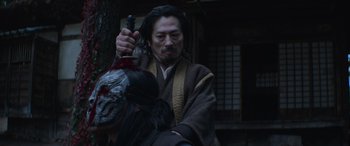 Movie still from “Mortal Kombat” (2021), directed by Simon McQuoid – A man holding a sword and a mask in his hand; Close Up shot, Low angle