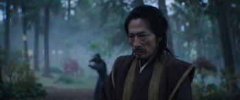 Movie still from “Mortal Kombat” (2021), directed by Simon McQuoid – A man in a robe standing in front of a tree; Medium shot, Over the shoulder angle