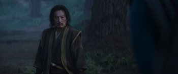 Movie still from “Mortal Kombat” (2021), directed by Simon McQuoid – A man with a sword standing in front of a tree; Medium shot, Low angle