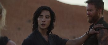 Movie still from “Mortal Kombat” (2021), directed by Simon McQuoid – A man with long black hair and a black shirt; Close Up shot, Over the shoulder angle