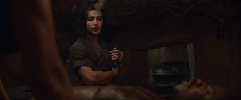 Movie still from “Mortal Kombat” (2021), directed by Simon McQuoid – A young man holding a knife in a dark room; Medium shot, Over the shoulder angle