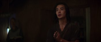 Movie still from “Mortal Kombat” (2021), directed by Simon McQuoid – A man with long black hair is holding a rosary; Close Up shot, Over the shoulder angle