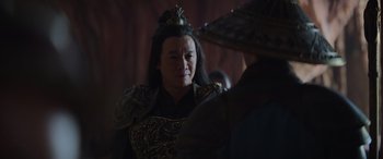 Movie still from “Mortal Kombat” (2021), directed by Simon McQuoid – An older woman wearing a black and gold dress; Close Up shot, Over the shoulder angle