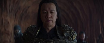 Movie still from “Mortal Kombat” (2021), directed by Simon McQuoid – A man with long black hair wearing a black and gold jacket; Close Up shot, Over the shoulder angle