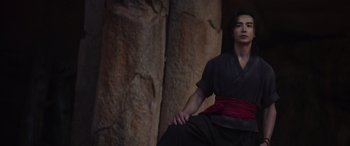 Movie still from “Mortal Kombat” (2021), directed by Simon McQuoid – A man sitting in front of a stone wall; Medium shot, Low angle