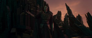 Movie still from “Mortal Kombat” (2021), directed by Simon McQuoid – A woman dressed in a costume standing in front of a stone wall; Medium shot, High angle