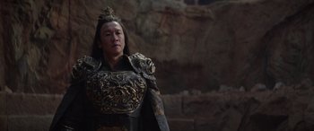 Movie still from “Mortal Kombat” (2021), directed by Simon McQuoid – A man in a costume standing in front of a stone wall; Medium shot, Low angle