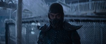 Movie still from “Mortal Kombat” (2021), directed by Simon McQuoid – A man wearing a helmet and armor stands in front of a fence; Medium shot, Low angle