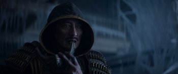 Movie still from “Mortal Kombat” (2021), directed by Simon McQuoid – A man in a hooded jacket holding a knife in his mouth; Close Up shot, Over the shoulder angle