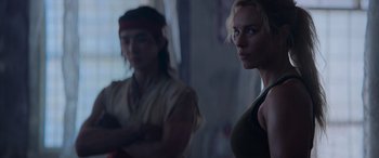 Movie still from “Mortal Kombat” (2021), directed by Simon McQuoid – A woman standing next to a man in a dark room; Medium shot, Over the shoulder angle