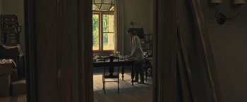 Movie still from “Mother!” (2017), directed by Darren Aronofsky – A person standing at a table in a room; Wide shot, High angle