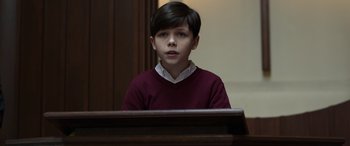 Movie still from “Mr. Harrigan's Phone” (2022), directed by John Lee Hancock – A boy in a red shirt is sitting at a podium; Close Up shot, Low angle