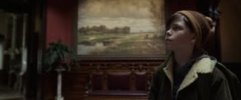 Movie still from “Mr. Harrigan's Phone” (2022), directed by John Lee Hancock – A man standing in front of a painting of a golf course; Medium shot, Low angle