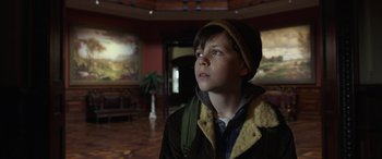 Movie still from “Mr. Harrigan's Phone” (2022), directed by John Lee Hancock – A boy in a hat and jacket looking up; Medium shot, Low angle