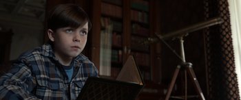 Movie still from “Mr. Harrigan's Phone” (2022), directed by John Lee Hancock – A young boy sitting in front of a book in a library; Close Up shot, High angle