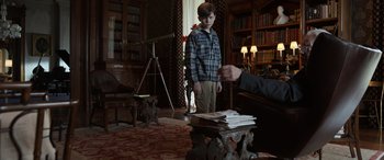 Movie still from “Mr. Harrigan's Phone” (2022), directed by John Lee Hancock – A boy standing next to a stack of papers; Medium shot, Over the shoulder angle