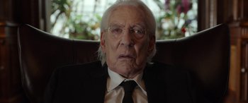 Movie still from “Mr. Harrigan's Phone” (2022), directed by John Lee Hancock – An old man wearing a suit and tie sitting in a chair; Close Up shot, Low angle