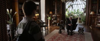 Movie still from “Mr. Harrigan's Phone” (2022), directed by John Lee Hancock – An older man sitting in a chair in a living room; Wide shot, Over the shoulder angle