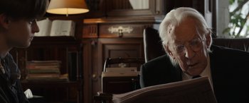 Movie still from “Mr. Harrigan's Phone” (2022), directed by John Lee Hancock – An older man sitting in a chair in front of a bookshelf; Close Up shot, Over the shoulder angle