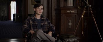 Movie still from “Mr. Harrigan's Phone” (2022), directed by John Lee Hancock – A young man sitting in a chair in a room; Medium shot, Over the shoulder angle