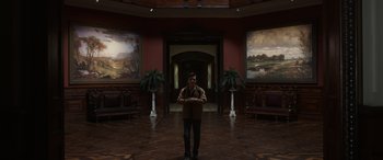 Movie still from “Mr. Harrigan's Phone” (2022), directed by John Lee Hancock – A man standing in front of two paintings in a room; Wide shot, Low angle