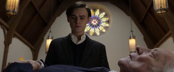 Movie still from “Mr. Harrigan's Phone” (2022), directed by John Lee Hancock – A man in a suit and tie in front of a stained glass window; Medium shot, Low angle