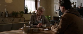 Movie still from “Mr. Harrigan's Phone” (2022), directed by John Lee Hancock – An older woman sitting at a table with a cup of coffee; Medium shot, Over the shoulder angle