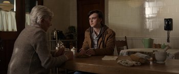 Movie still from “Mr. Harrigan's Phone” (2022), directed by John Lee Hancock – A man sitting at a wooden table in front of another man; Medium shot, Over the shoulder angle