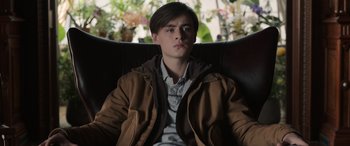 Movie still from “Mr. Harrigan's Phone” (2022), directed by John Lee Hancock – A young man sitting in a chair wearing a brown jacket; Medium shot, Over the shoulder angle