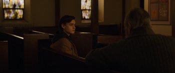 Movie still from “Mr. Harrigan's Phone” (2022), directed by John Lee Hancock – A young man sitting in a pew in front of a stained glass window; Medium shot, Over the shoulder angle