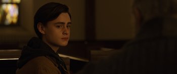 Movie still from “Mr. Harrigan's Phone” (2022), directed by John Lee Hancock – A man sitting in front of a microphone in a dark room; Close Up shot, Over the shoulder angle