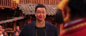 Movie still from “Mulan” (2020), directed by Niki Caro – An older man wearing a blue jacket and a black hat; Close Up shot, Over the shoulder angle