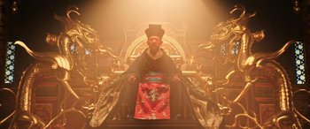 Movie still from “Mulan” (2020), directed by Niki Caro – A man sitting on top of a throne in front of a golden background; Wide shot, Low angle