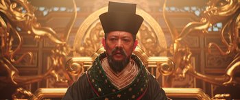 Movie still from “Mulan” (2020), directed by Niki Caro – A man with a long beard wearing a black hat; Medium shot, Low angle